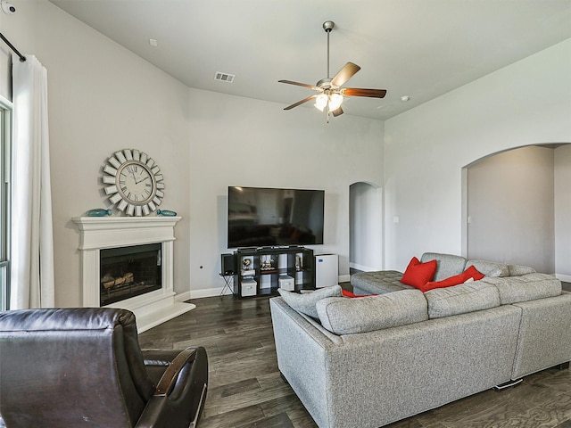 9713 Excursion Dr, Little Elm, TX 75068 - living room with arched walkways, a ceiling fan, dark wood-type flooring, a fireplace with raised hearth, and baseboards