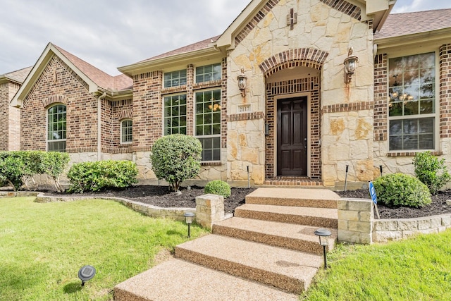 2117 Torin St, Lewisville, TX 75056 - doorway to property featuring stone siding, a shingled roof, brick siding, and a yard