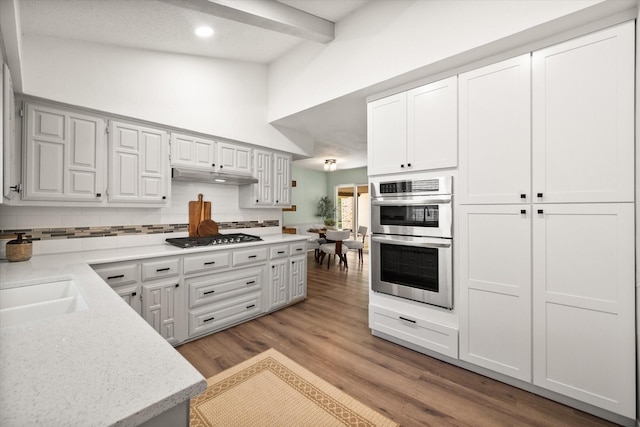 626 Pebblecreek Dr, Garland, TX 75040 - kitchen with stainless steel appliances, tasteful backsplash, under cabinet range hood, beamed ceiling, and light wood-style floors