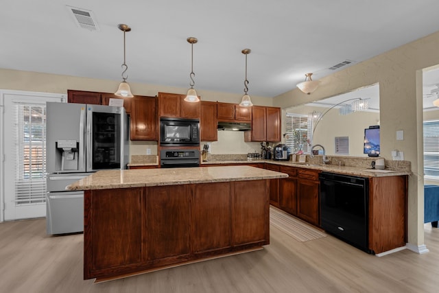 7413 Dana Ln, North Richland Hills, TX 76182 - kitchen with black appliances, light wood-style flooring, under cabinet range hood, a center island, and hanging light fixtures