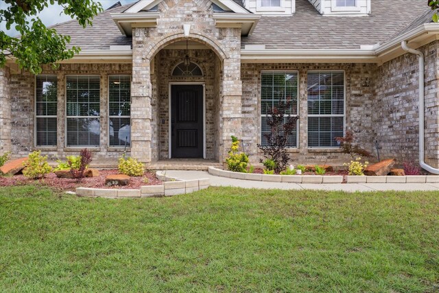 10237 Red Bluff Ln, Fort Worth, TX 76177 - view of exterior entry featuring a lawn, a shingled roof, and brick siding
