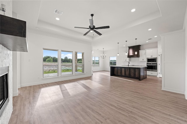 7009 Ranch View Pl, Springtown, TX 76082 - unfurnished living room with a tray ceiling, a glass covered fireplace, recessed lighting, light wood-style flooring, and a sink