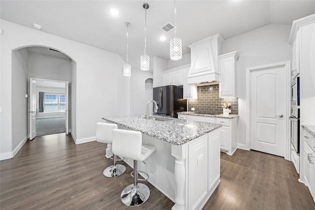558 Lily St, Crowley, TX 76036 - kitchen featuring arched walkways, black appliances, custom range hood, dark wood-type flooring, and an island with sink