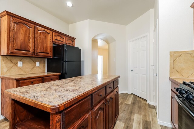 1012 Fairweather Dr, Fort Worth, TX 76120 - kitchen featuring black appliances, arched walkways, light wood-type flooring, decorative backsplash, and light countertops