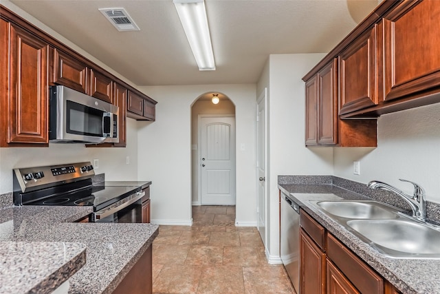 7660 Hollow Forest Dr, Fort Worth, TX 76123 - kitchen with appliances with stainless steel finishes, baseboards, a sink, arched walkways, and light stone finish flooring