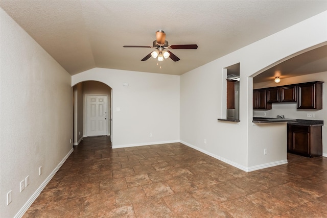 7660 Hollow Forest Dr, Fort Worth, TX 76123 - unfurnished living room with arched walkways, ceiling fan, dark stone finish floors, baseboards, and lofted ceiling