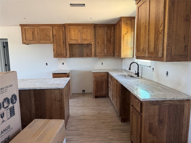 1009 Brown Ct, Poolville, TX 76487 - kitchen with a sink, wood finished floors, brown cabinetry, and light stone countertops
