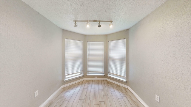 928 Thistle Ridge Ln, Arlington, TX 76017 - unfurnished room featuring a textured wall, track lighting, baseboards, light wood-type flooring, and a textured ceiling