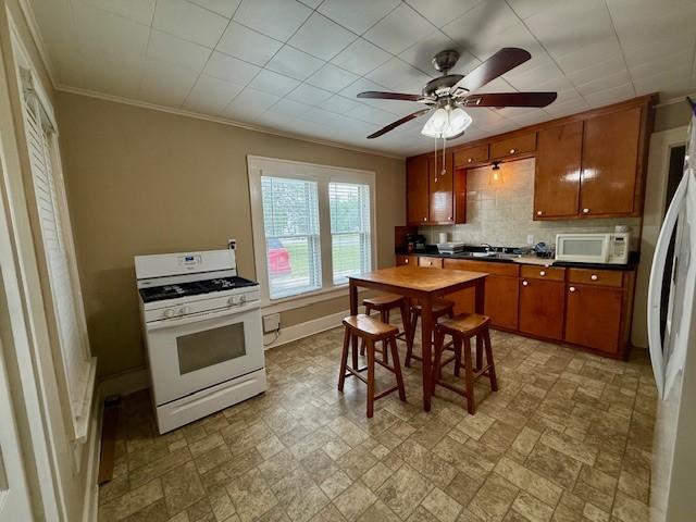 322 E Division St, Muenster, TX 76252 - kitchen featuring white appliances, decorative backsplash, brown cabinetry, dark countertops, and baseboards
