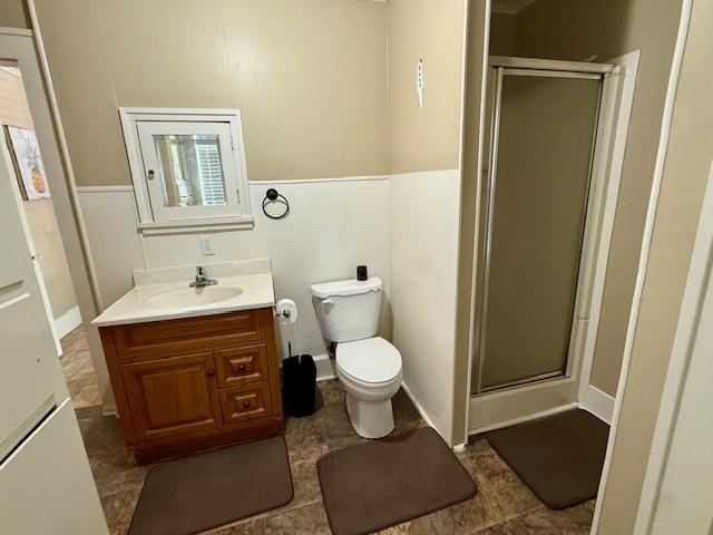 322 E Division St, Muenster, TX 76252 - bathroom with vanity, a shower stall, toilet, wainscoting, and tile walls