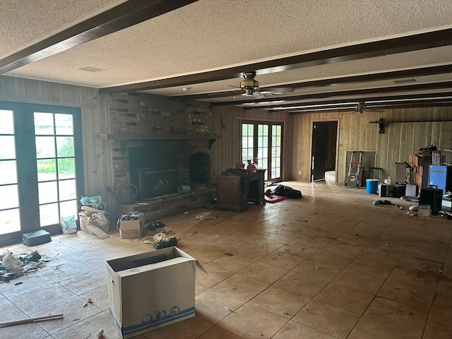 3182 E US Highway 84, Palestine, TX 75801 - unfurnished living room featuring a textured ceiling, wood walls, beam ceiling, ceiling fan, and a fireplace