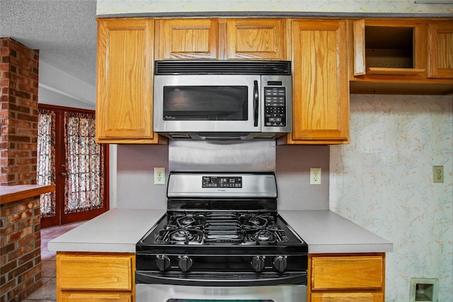 2025 Sancerre Ln, Carrollton, TX 75007 - kitchen featuring appliances with stainless steel finishes, light countertops, wallpapered walls, brown cabinets, and a textured ceiling