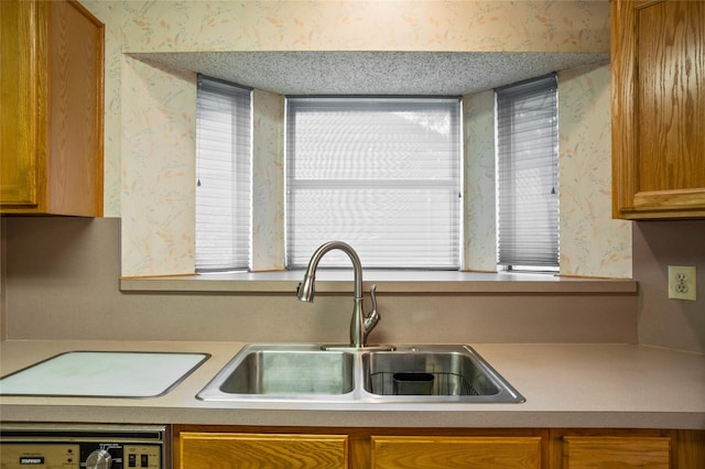 2025 Sancerre Ln, Carrollton, TX 75007 - kitchen with wallpapered walls, a sink, brown cabinetry, light countertops, and washer / clothes dryer