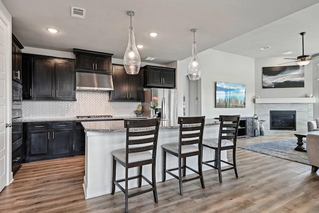 3200 Julian St, Mansfield, TX 76063 - kitchen featuring appliances with stainless steel finishes, under cabinet range hood, backsplash, light stone countertops, and wood finished floors