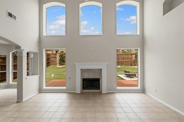 204 Forestview Rd, Hickory Creek, TX 75065 - unfurnished living room with a high ceiling, a tiled fireplace, plenty of natural light, ornate columns, and light tile patterned floors