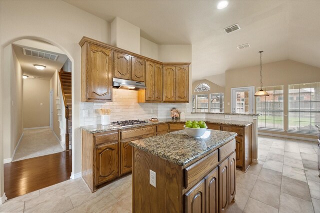 304 Adobe Lilly Ct, Mansfield, TX 76063 - kitchen featuring stainless steel gas stovetop, a peninsula, under cabinet range hood, brown cabinets, and light stone countertops