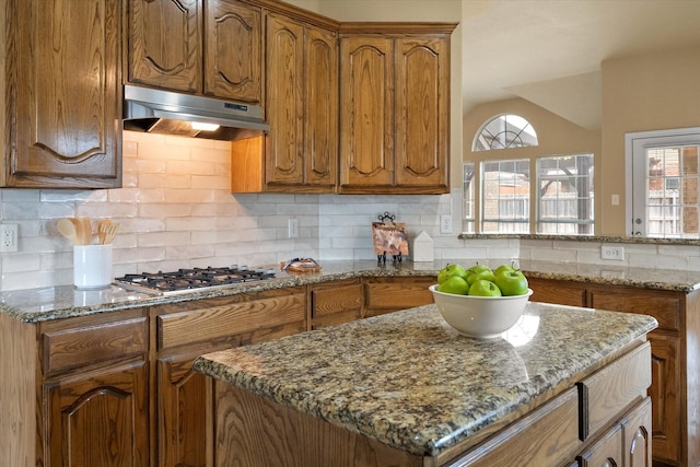 304 Adobe Lilly Ct, Mansfield, TX 76063 - kitchen featuring under cabinet range hood, stainless steel gas cooktop, brown cabinetry, and stone counters