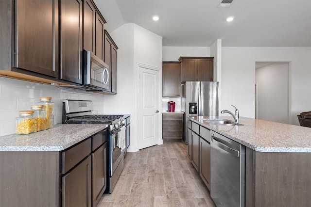 3004 Aransas Ave, Aubrey, TX 76227 - kitchen featuring stainless steel appliances, a sink, dark brown cabinets, light wood finished floors, and an island with sink