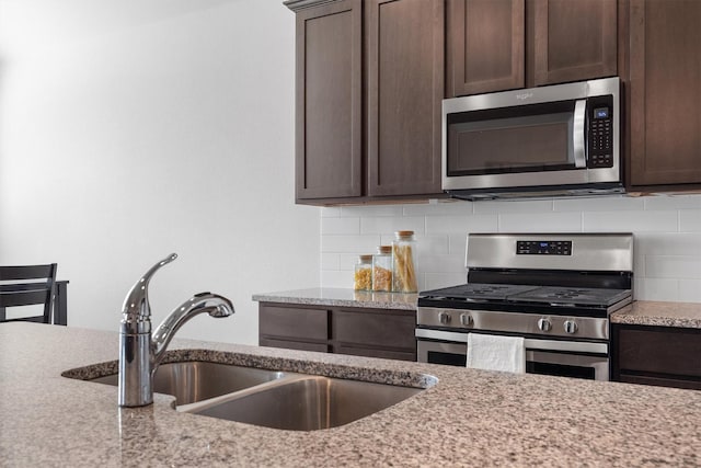3004 Aransas Ave, Aubrey, TX 76227 - kitchen featuring appliances with stainless steel finishes, dark brown cabinetry, a sink, and backsplash