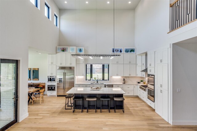 1209 Hicks Trl, Lucas, TX 75002 - kitchen with stainless steel appliances, a towering ceiling, a sink, a kitchen bar, and light wood finished floors
