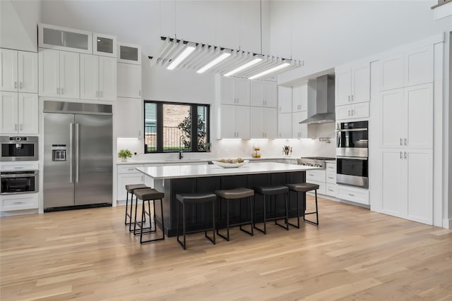 1209 Hicks Trl, Lucas, TX 75002 - kitchen with stainless steel appliances, wall chimney exhaust hood, a breakfast bar, a sink, and light wood-type flooring