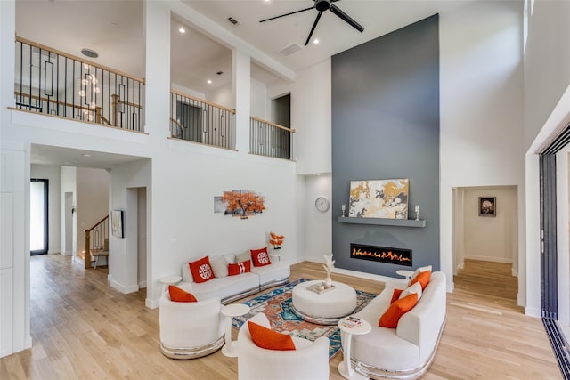 1209 Hicks Trl, Lucas, TX 75002 - living area featuring a high ceiling, ceiling fan, wood finished floors, a warm lit fireplace, and stairs