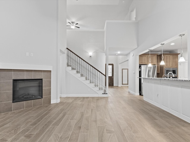 2508 Bunker Hill Dr, Burleson, TX 76028 - unfurnished living room with light wood-style floors, ceiling fan, stairway, a high ceiling, and a tiled fireplace