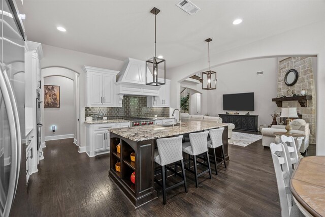 8249 Treemont Pl, Frisco, TX 75034 - kitchen with arched walkways, white cabinetry, tasteful backsplash, an island with sink, and light stone counters