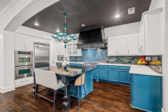 7905 Strathmill Dr, The Colony, TX 75056 - kitchen featuring premium range hood, built in appliances, blue cabinets, a kitchen breakfast bar, and dark wood finished floors