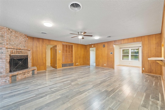 201 Palestine St, Coleman, TX 76834 - unfurnished living room featuring a ceiling fan, a textured ceiling, a brick fireplace, wooden walls, and wood finished floors