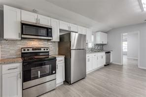 128 Stephens St, Waxahachie, TX 75165 - kitchen featuring appliances with stainless steel finishes, tasteful backsplash, light wood finished floors, white cabinetry, and vaulted ceiling