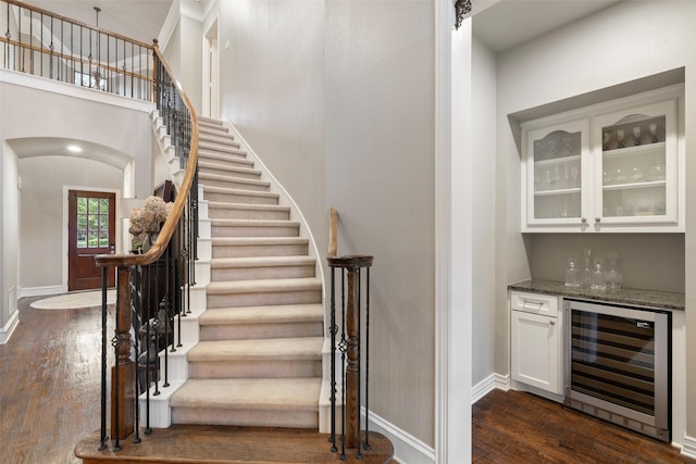 1229 Comanche Dr, Allen, TX 75013 - stairway with beverage cooler, a dry bar, wood finished floors, a high ceiling, and arched walkways