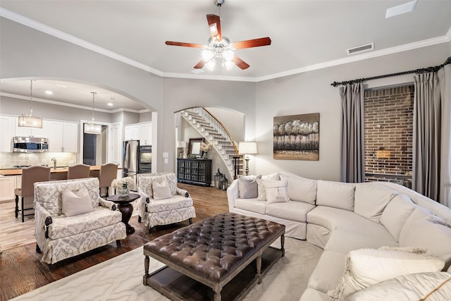 1229 Comanche Dr, Allen, TX 75013 - living area featuring arched walkways, light wood-type flooring, ceiling fan, stairs, and ornamental molding