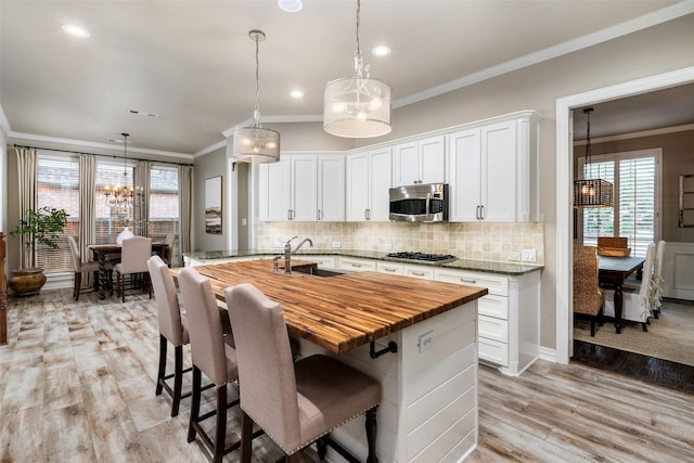 1229 Comanche Dr, Allen, TX 75013 - kitchen featuring appliances with stainless steel finishes, butcher block countertops, ornamental molding, light wood finished floors, and tasteful backsplash