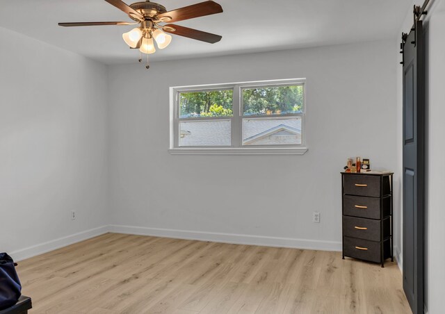 7718 Royal Ln Unit 214, Dallas, TX 75230 - unfurnished bedroom featuring a barn door, light wood finished floors, baseboards, and a ceiling fan