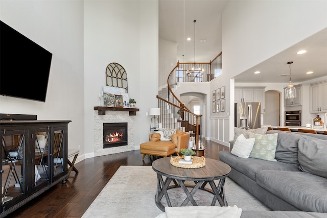 1008 Cason Falls Rd, Mckinney, TX 75071 - living area featuring arched walkways, a high ceiling, dark wood-type flooring, stairs, and a glass covered fireplace