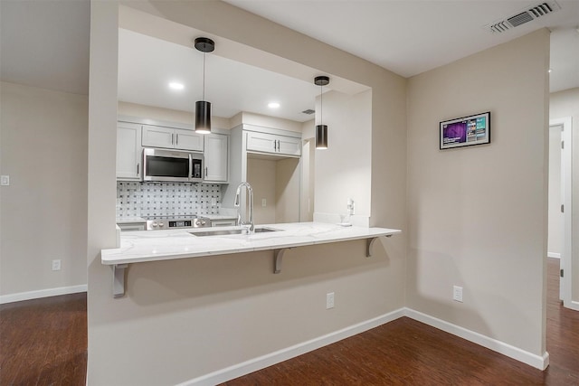 7013 Buttonwood Dr, Fort Worth, TX 76137 - kitchen featuring stainless steel microwave, a sink, a breakfast bar area, light stone countertops, and dark wood finished floors