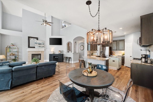 4710 Safe Harbour Dr, Arlington, TX 76016 - dining area with arched walkways, a chandelier, ceiling fan, light wood-style flooring, and a tiled fireplace