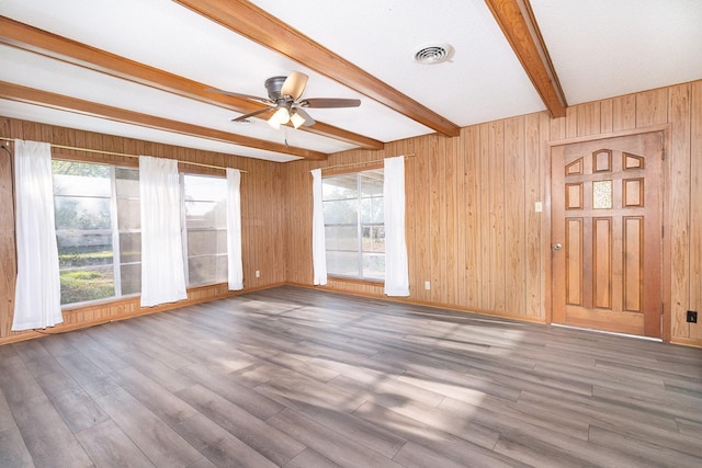 403 W China St, Brady, TX 76825 - unfurnished living room featuring a ceiling fan, beamed ceiling, plenty of natural light, wood finished floors, and wooden walls