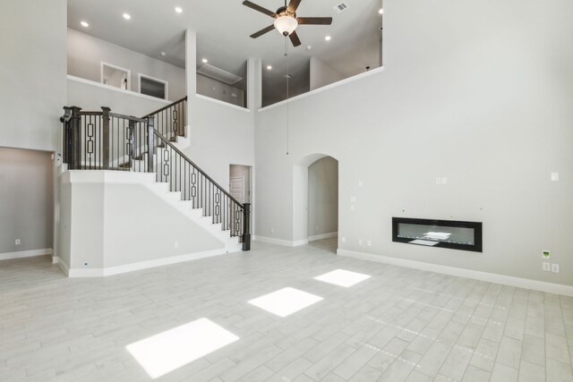 1105 Alaska, Forney, TX 75126 - unfurnished living room with ceiling fan, arched walkways, a glass covered fireplace, baseboards, and a towering ceiling