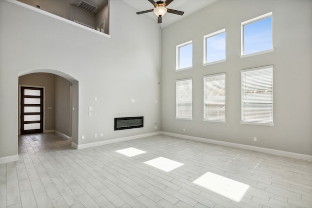 1105 Alaska, Forney, TX 75126 - unfurnished living room featuring a high ceiling, a ceiling fan, arched walkways, a glass covered fireplace, and baseboards