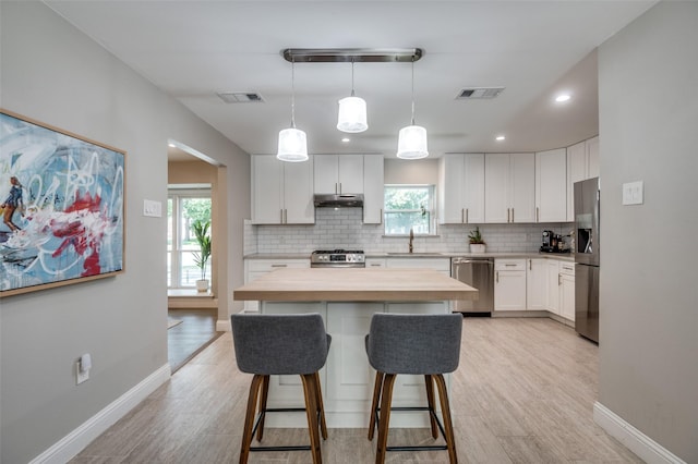3385 Northaven Rd, Dallas, TX 75229 - kitchen featuring stainless steel appliances, a sink, under cabinet range hood, wood counters, and decorative backsplash
