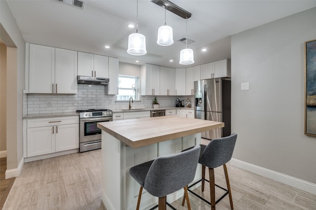 3385 Northaven Rd, Dallas, TX 75229 - kitchen featuring appliances with stainless steel finishes, under cabinet range hood, wood counters, a breakfast bar, and light wood-type flooring