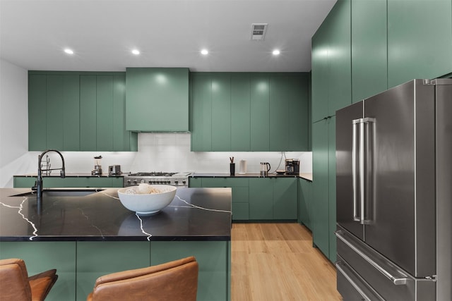 3941 Adrian Dr, Dallas, TX 75209 - kitchen with high quality fridge, green cabinets, wall chimney range hood, a sink, and light wood-style floors