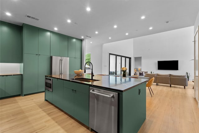3941 Adrian Dr, Dallas, TX 75209 - kitchen featuring green cabinetry, a sink, stainless steel appliances, a kitchen island with sink, and light wood-style flooring