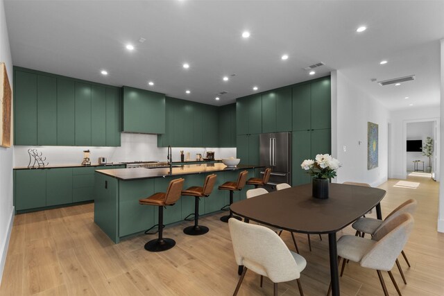 3941 Adrian Dr, Dallas, TX 75209 - kitchen featuring high end fridge, a center island with sink, light wood finished floors, green cabinets, and modern cabinets