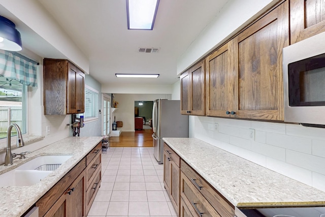 1803 Travis St, Garland, TX 75042 - kitchen featuring stainless steel appliances, decorative backsplash, light tile patterned flooring, light stone counters, and brown cabinetry