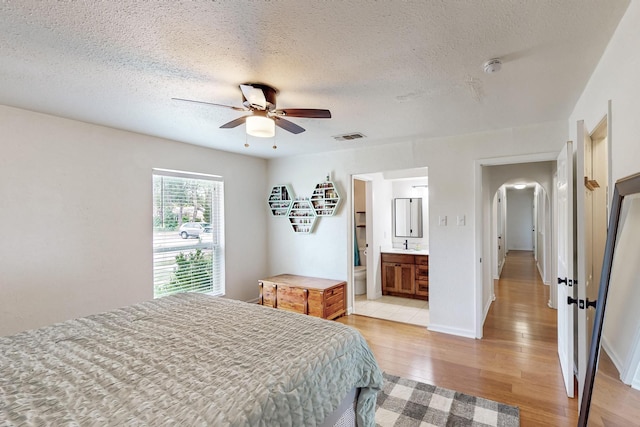 1803 Travis St, Garland, TX 75042 - bedroom featuring arched walkways, light wood-style floors, a textured ceiling, ceiling fan, and ensuite bathroom