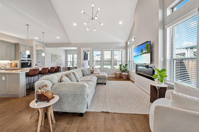 3580 Spruce Hills St, Frisco, TX 75033 - living room featuring high vaulted ceiling, wood finished floors, healthy amount of natural light, a glass covered fireplace, and a chandelier
