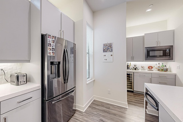 1813 Park Ave Unit 204, Dallas, TX 75215 - kitchen with appliances with stainless steel finishes, gray cabinetry, wine cooler, backsplash, and light wood-style flooring